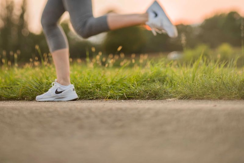 A runner's legs mid-stride on a grass verge in morning light